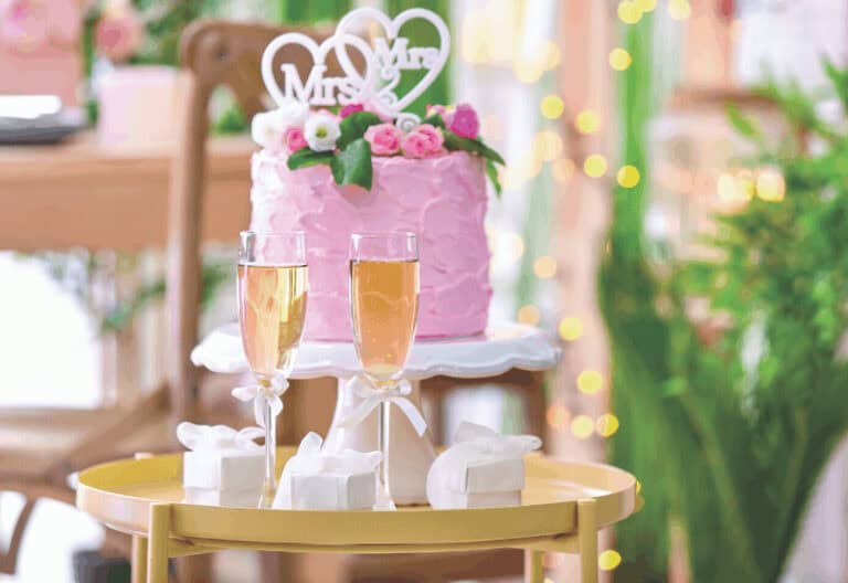 2 tiered pink wedding cake with a bouble heart topper that says mrs. & mrs.