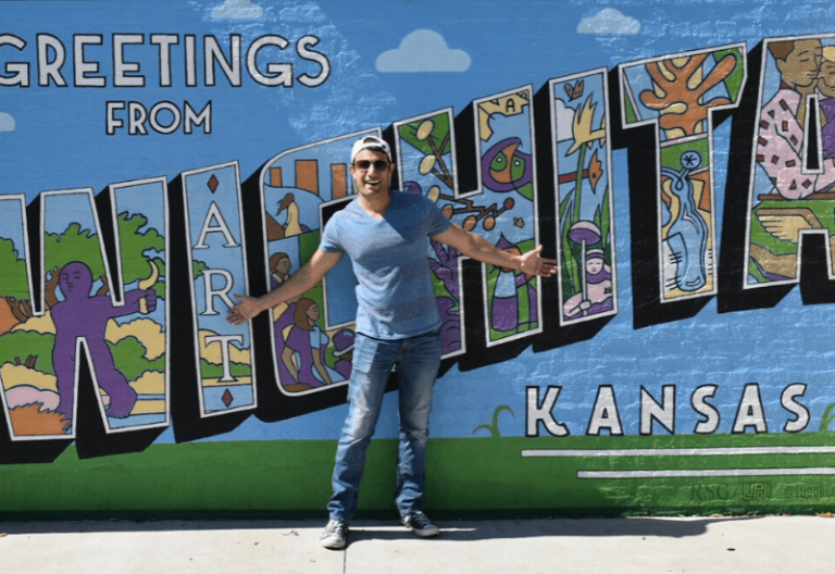 Joey Amato parado frente a un mural que dice Saludos desde Wichita Kansas