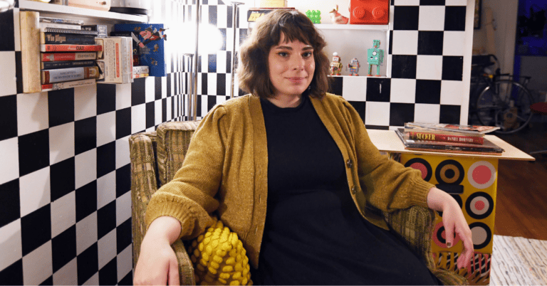 Sara Moseley sits in a green chair in front of a checkered wall.