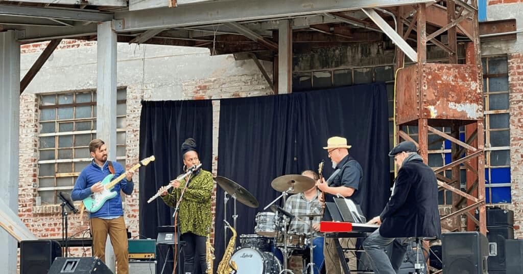Hope plays flute with band Gritty City Bang Bang outside on stage.