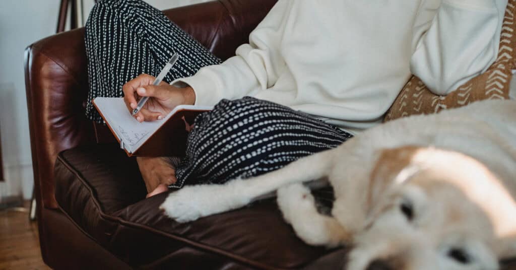 Person writing while white dog naps. 7 Ways to Beat the Winter Blahs, via Pexel