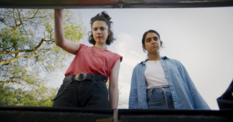 Margaret Qualley, Geraldine Viswanathan in Drive-Away Dolls looking down into a trunk with unsettled expressions