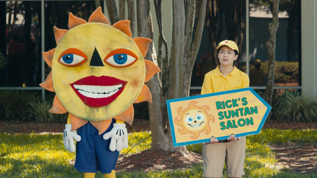 De izquierda a derecha: Ataviado con un aterrador disfraz de sol, Egghead (Louis Tomeo) ayuda a anunciar un salón de bronceado con su mejor amiga, Twinkie (Sabrina Jie-A-Fa).