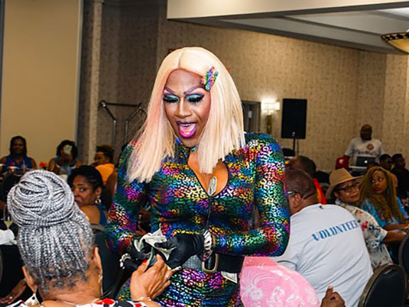 Pride events image, Black drag performer in rainbow jumpsuit takes tips from excited patrons