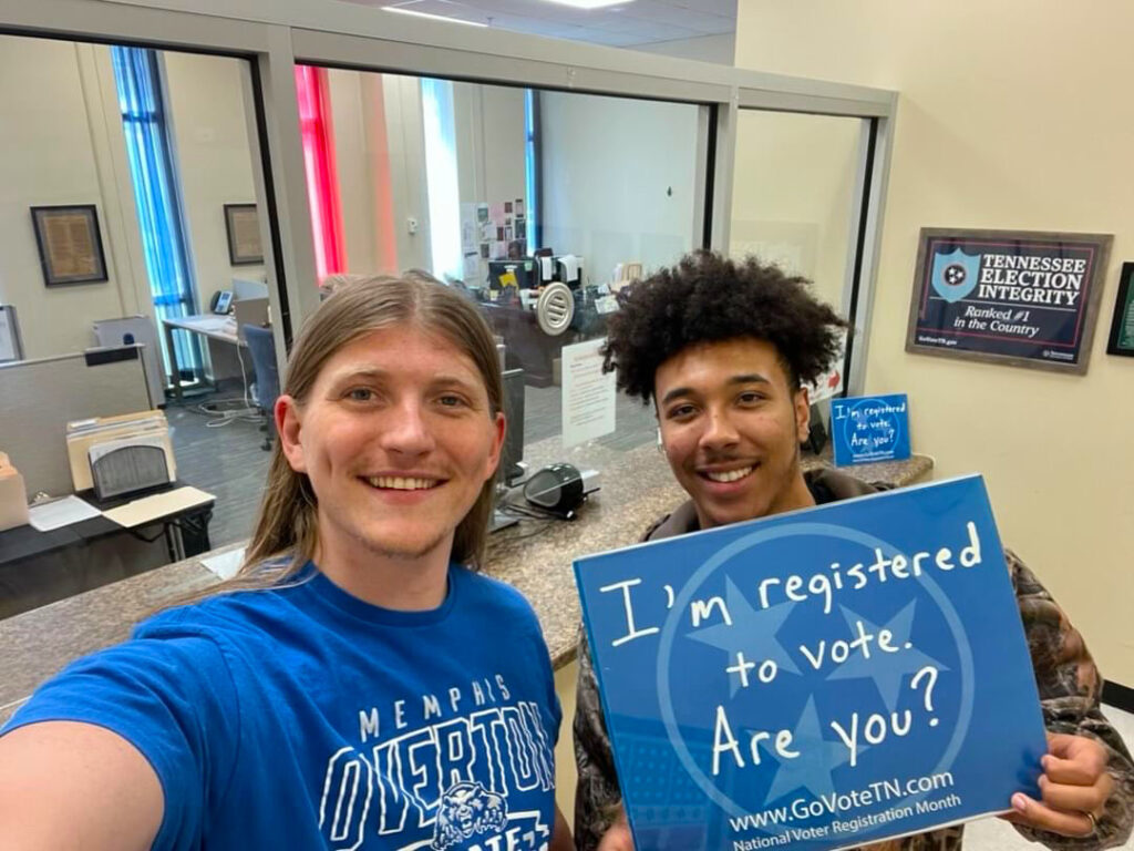 Noah Nordstrom with community member. Both wear blue and hold a sign that reads "I'm registered to vote. Are you?"