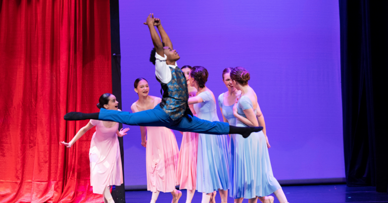 Black transmasc dancer leaps in front of four other dancers on stage