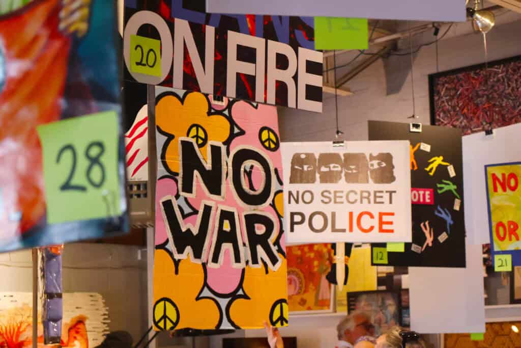 Protest signs with messages like "NO WAR" and "NO SECRET POLICE" hang in an indoor space. — focuslgbt.com