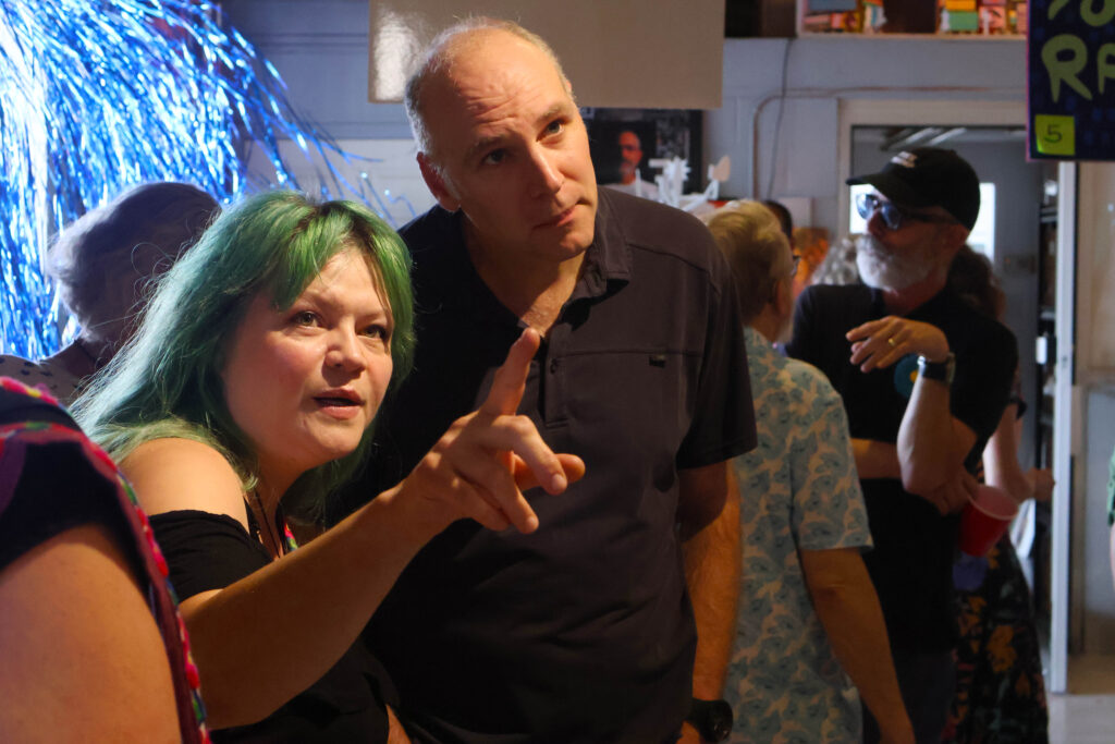Two people in conversation at an indoor event, one with green hair and the other with a bald head. — focuslgbt.com