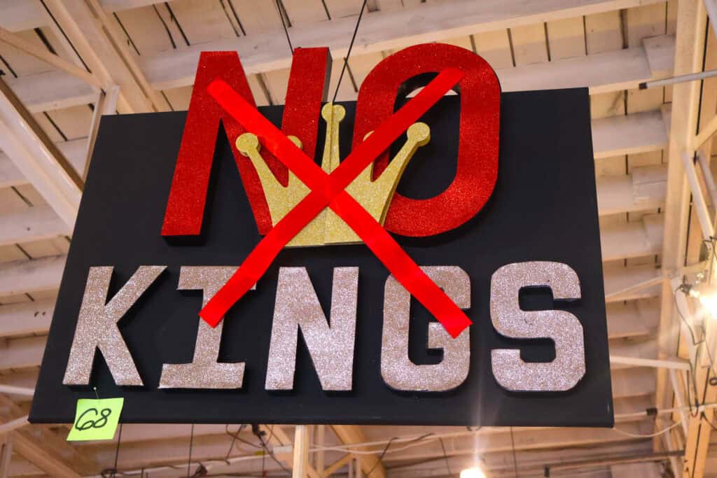 No Kings sign with red crossed-out clock and gold crown, hanging indoors. — focuslgbt.com