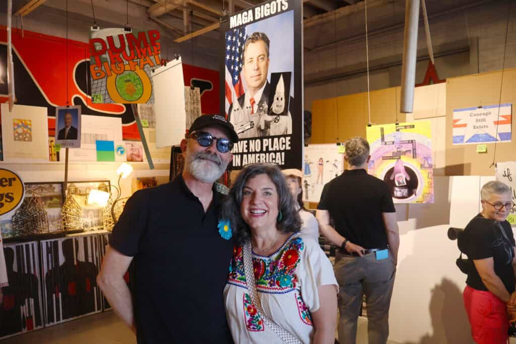 Two people smile at an art exhibit in Memphis, one wearing sunglasses and a blue flower pin. — focuslgbt.com