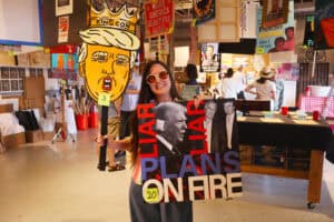 Person holding a protest sign with Donald Trump and Joe Biden images at an indoor event. — focuslgbt.com