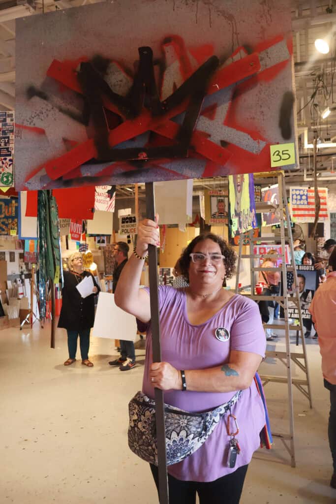 Person holding a protest sign with a red and black spray-painted symbol. — focuslgbt.com