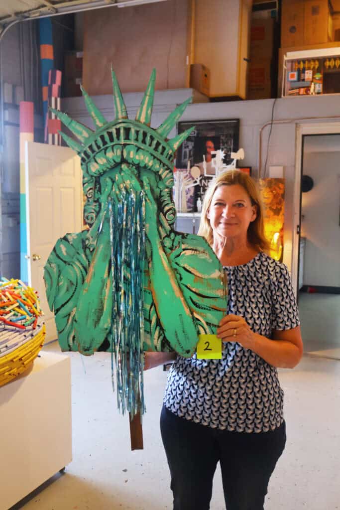 Woman holding a large green Statue of Liberty cutout with blue streamers. — focuslgbt.com