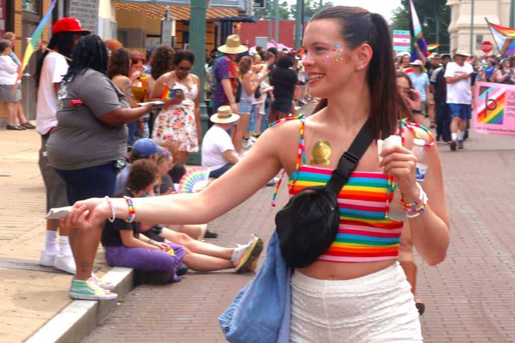 Person in rainbow-striped top hands out beads at Pride parade in Memphis. — focuslgbt.com
