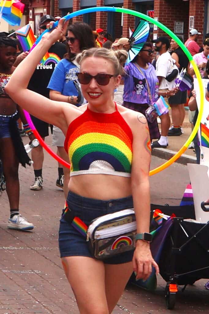 Person in rainbow crop top and shorts holding a hula hoop at Pride parade. — focuslgbt.com