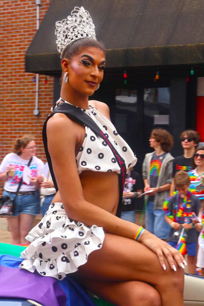 Performer in polka dot costume and crown sits on parade float during Pride event. — focuslgbt.com