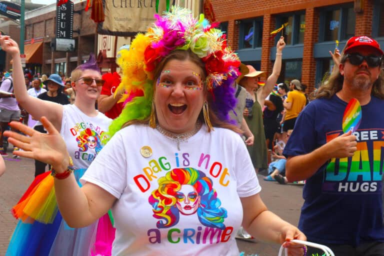 Person with rainbow-colored flower crown and a "Drag is not a crime" T-shirt at Pride parade. — focuslgbt.com