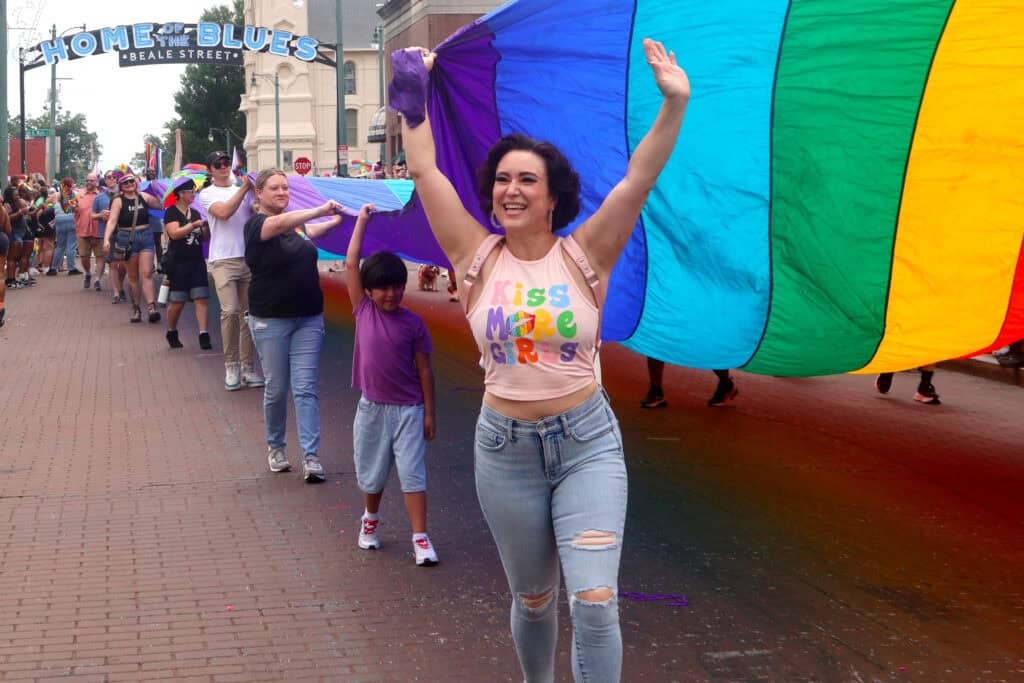 Performer in a crop top and ripped jeans waves under a rainbow flag at Pride parade. — focuslgbt.com