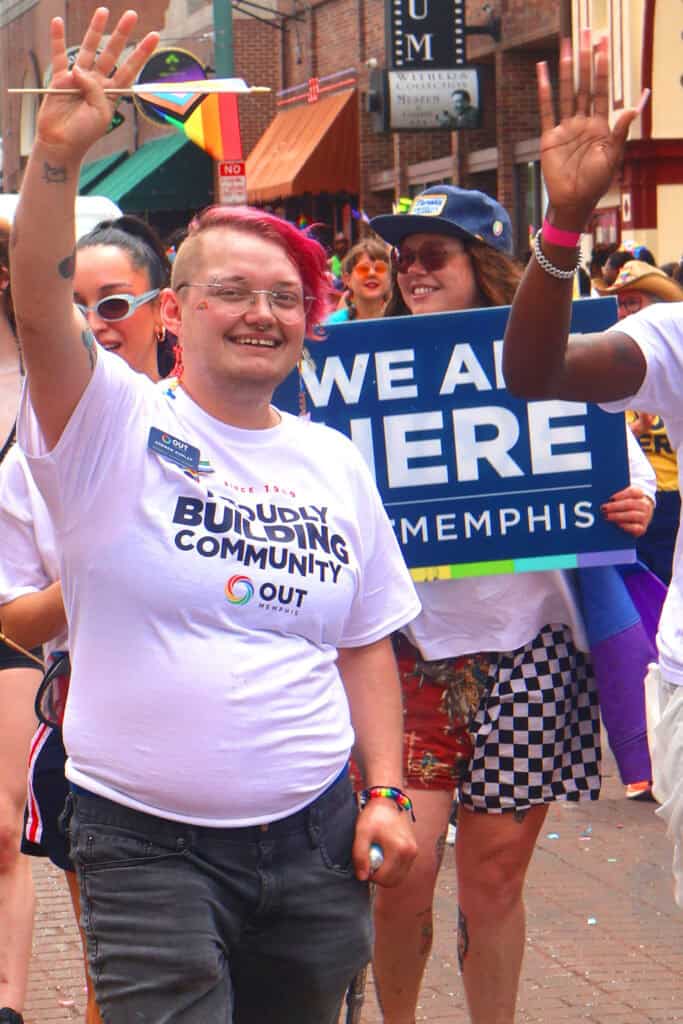 Person with pink hair and glasses waving at Pride parade in Memphis. — focuslgbt.com