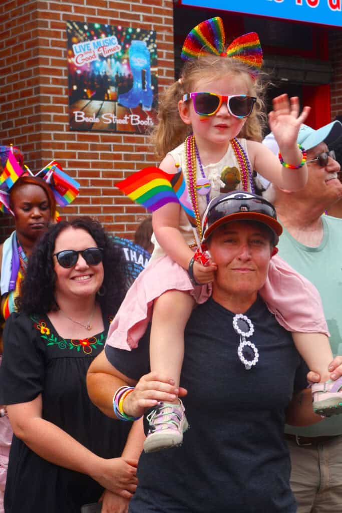 Child with rainbow bow and sunglasses waves at Pride parade in Memphis. — focuslgbt.com