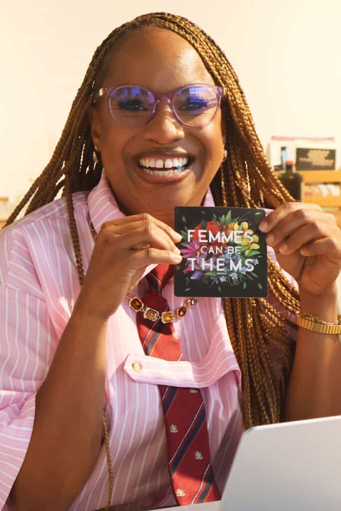 Person with braided hair and glasses holding a Pride card in an office. — focuslgbt.com