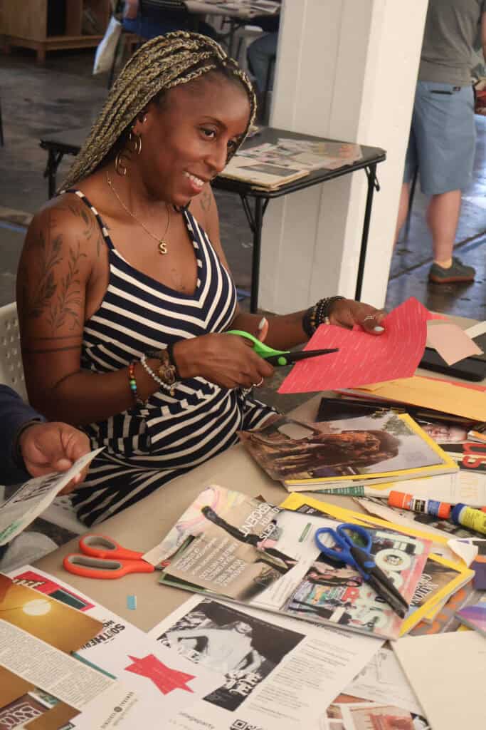 Woman with braided hair and tattoos cuts paper at table with craft supplies. — focuslgbt.com