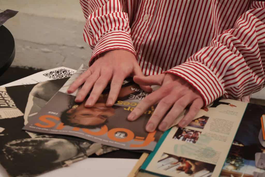 Person in red-striped shirt flipping through magazines on table. — focuslgbt.com