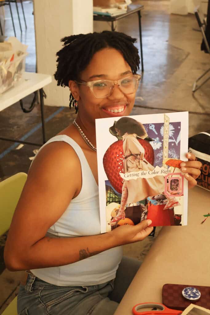 Woman with glasses and dreadlocks holding a colorful magazine at a table. — focuslgbt.com