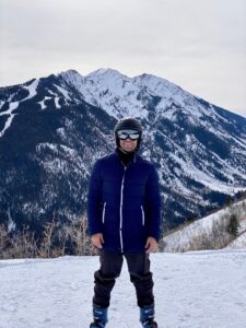 Person in ski gear stands on snowy mountain slope with snow-covered peaks behind. — focuslgbt.com