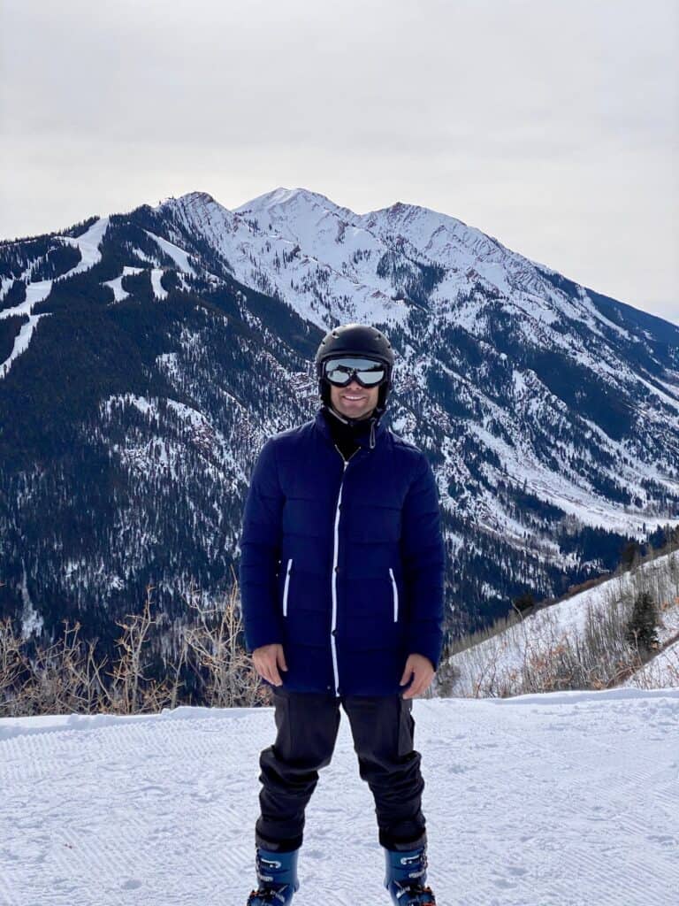 Person in ski gear stands on snowy mountain slope with snow-covered peaks behind. — focuslgbt.com